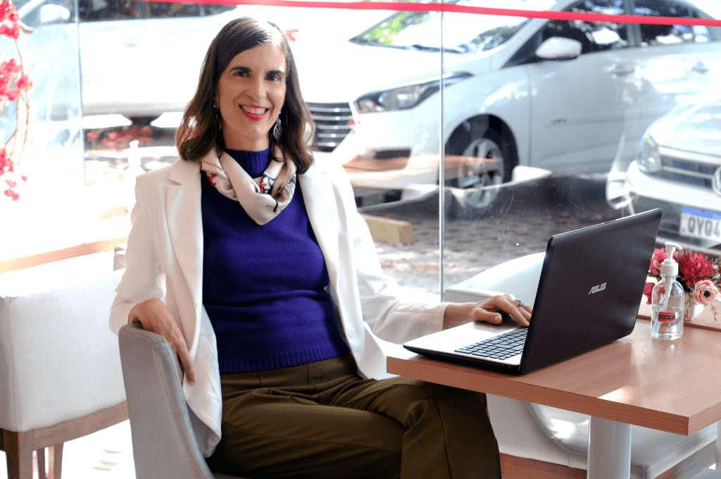 mulher sorridente sentada numa mesa com seu notebook