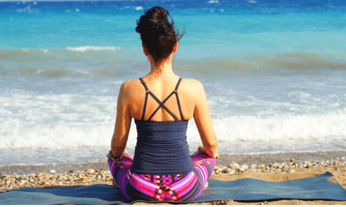 mulher sentada na areia da praia meditando